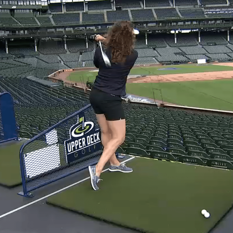 Woman hitting a golf ball from a temporary tee in the upper deck of Wrigley Field